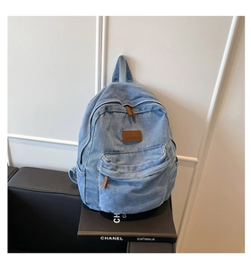 Detailed view of light blue washed denim backpack with brown leather tags and zippers