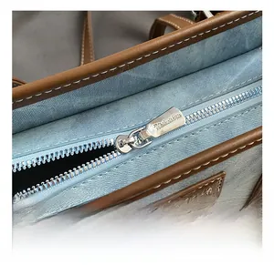 Close-up of silver metal zipper and branded plaque on blue lace tote bag details