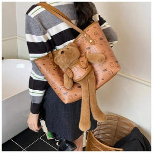 Brown leather tote bag featuring a cute plush bear pendant and cartoon bear pattern details