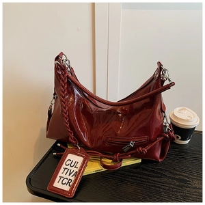 Close-up of wine red hobo bag with woven strap and glossy texture on black wooden surface