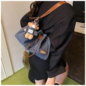 Detail of denim tote bag with leather strap and a cute teddy bear plush charm