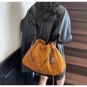 Detail of tan suede tote bag with drawstring texture and thin shoulder strap worn by model