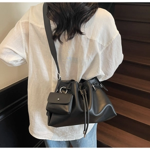 Detail of minimalist black drawstring bucket bag with mini pouch on a white linen shirt