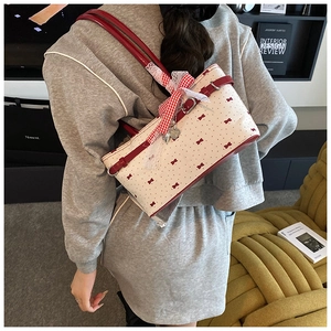 Détail du sac cabas blanc avec nœuds rouges, breloque cœur et bandoulière en cuir rouge
