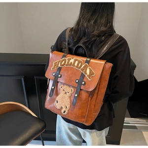 Detail view of vintage brown leather backpack with plush bear and HOLIDAY patch on the back