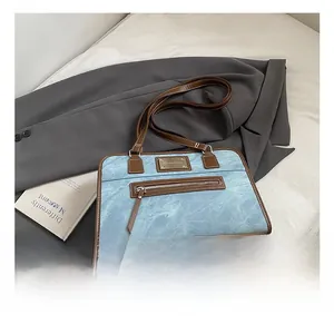 Detail of vintage washed denim underarm bag featuring brown leather trim and front zipper
