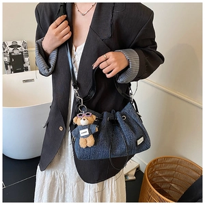 Detail of denim bucket bag with black leather straps and a cute plush bear charm