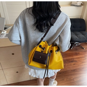 Detail of yellow drawstring bucket bag with a brown envelope charm on a crossbody strap
