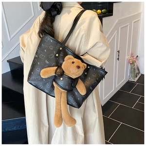 Detail of black tote bag featuring a cartoon bear print and a plush teddy bear charm