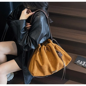 Detail of a large amber pleated tote bag with dark leather straps and metal brand logo