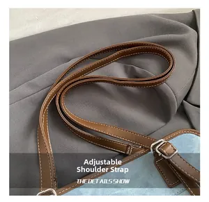 Detail of adjustable brown faux leather shoulder strap with silver buckle on denim bag