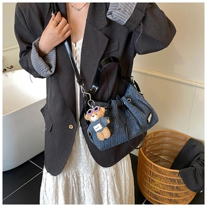 Detail of denim bucket bag with black leather strap and brown teddy bear charm accessory