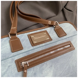 Detail of denim shoulder bag featuring contrast stitching and a gold logo plate