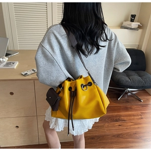 Detail of yellow drawstring bucket bag with brown leather strap and small coin purse accessory