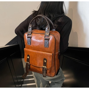 Detailed back view of a vintage brown leather backpack worn by a model on dark stairs