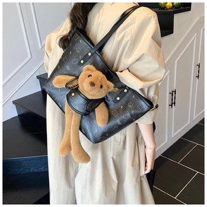 Detail of black teddy bear tote with gold rivets and a plush bear pendant in leather vest