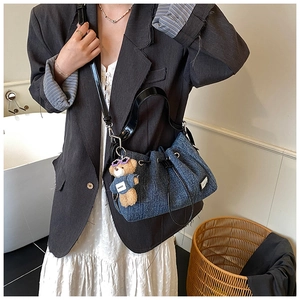 Detail of blue denim drawstring bucket bag with black leather straps and cartoon bear charm