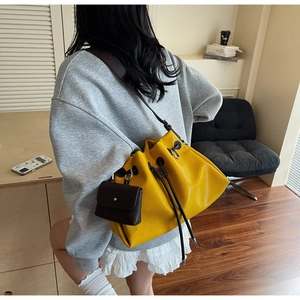 Detail of yellow drawstring bucket bag and mini brown pouch shown from a side back view