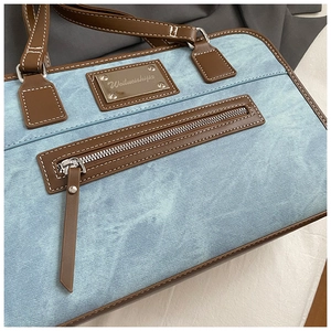 Close-up of light blue denim fabric and brown leather handle on a chic shoulder bag