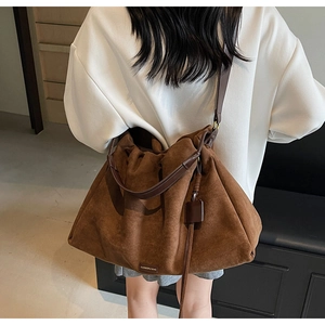 Detail of a large brown suede tote bag showing the texture and leather strap on a model