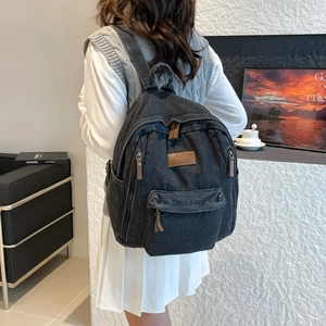 Fashionable black washed denim backpack with leather accents worn by a model in casual setting