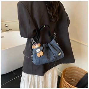 Detail of blue denim bucket bag with drawstring closure and cute teddy bear charm pendant