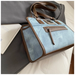 Detail of blue denim shoulder bag featuring brown leather trim and metal zip pocket