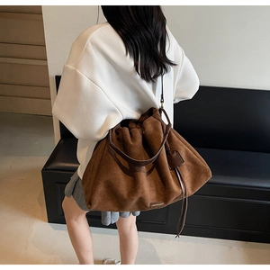 Brown suede tote bag with drawstring closure and metal brand label on a model's shoulder
