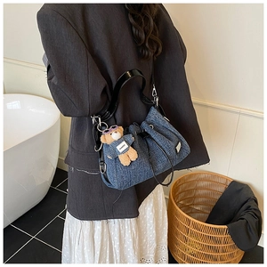 Detail of blue denim bucket bag with black leather straps and a cute bear charm accessory
