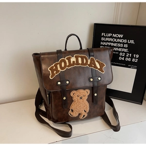 Detail view of brown vintage backpack featuring teddy bear patch and HOLIDAY embroidery