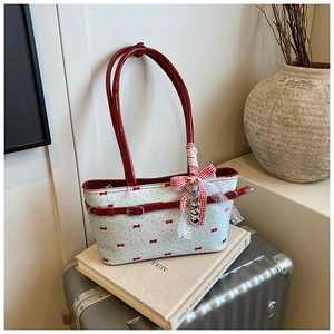 Détail d'un sac cabas blanc avec nœuds rouges, dentelle et breloque cœur argentée