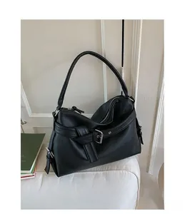 Detail of black pebbled leather tote bag featuring a silver metal buckle on a sofa