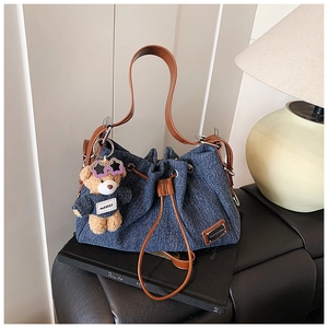 Detail of denim drawstring bucket bag with leather strap and plush bear charm