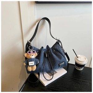 Detail of blue denim bucket bag with black leather strap and stylish teddy bear charm
