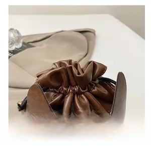 Detail of brown leather bucket bag showing drawstring closure and brass rivet accents