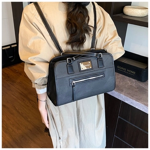 Detail of matte black shoulder bag featuring white contrast stitching and metal plaque