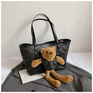 Detail of a black tote bag with plush bear charm and animal pattern on synthetic leather