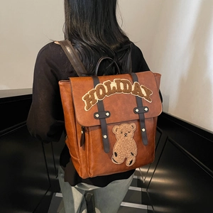 Vintage brown leather backpack with 'HOLIDAY' bear embroidery, worn by model on stairs