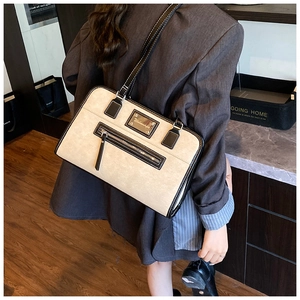 Detail of beige underarm bag with black trim and front zipper shown on a model's shoulder