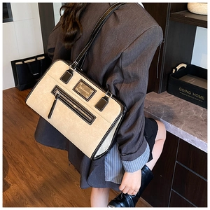Detail of a large beige shoulder bag with black trim and a front zipper pocket