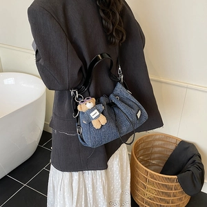Denim tote bag with black glossy strap and bear pendant worn by a model in a modern room