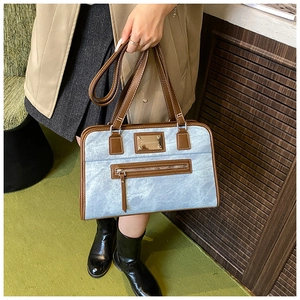 Detail of light blue denim texture shoulder bag with brown leather trim and metal logo