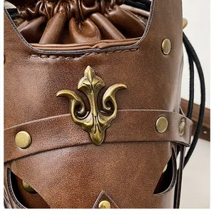Detail of brown lychee leather bag featuring a brass fleur-de-lis logo and metallic rivets