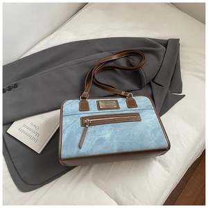 Detail of blue denim shoulder bag with brown leather trim and front zipper pocket