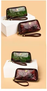 Close-up of floral embossed leather wristlet featuring golden metal zippers and charms