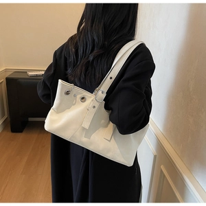 Detailed view of white leather shoulder bag with silver eyelets and adjustable buckle strap