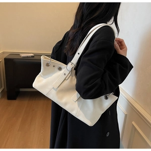 Detail view of cream leather shoulder bag with silver eyelets on female model