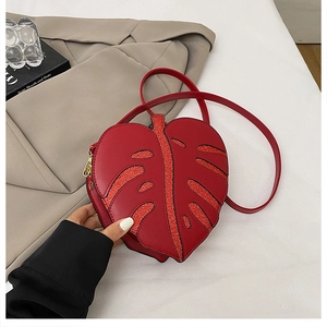 Detail of red leaf-shaped shoulder bag featuring glitter texture and golden metal zipper