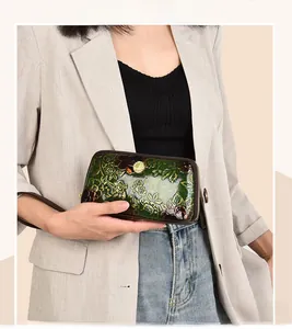 Detail of dark green leather clutch featuring embossed floral patterns and gold zipper