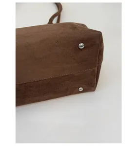 Detail des verstärkten Taschenbodens mit silbernen Metallfüßen auf braunem Wildleder